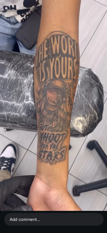 Benson Carlos black and gray astronaut tattoo with lettering on forearm in Hawaii.